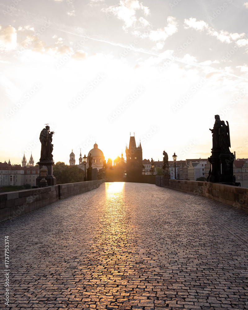 Obraz premium Stunning sunrise over Prague with warm golden light illuminating historic architecture, cobblestone streets, and iconic city landmarks in high-quality detail.