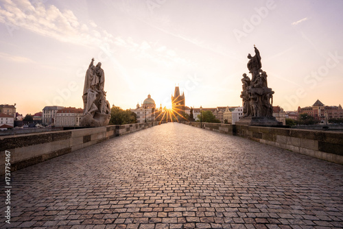 Stunning sunrise over Prague with warm golden light illuminating historic architecture, cobblestone streets, and iconic city landmarks in high-quality detail.