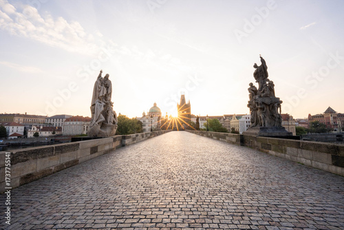 Stunning sunrise over Prague with warm golden light illuminating historic architecture, cobblestone streets, and iconic city landmarks in high-quality detail.