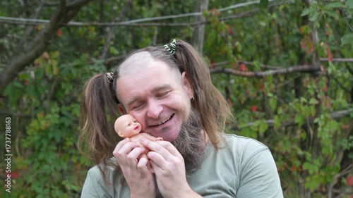 Funny bearded man with pigtails holding and playing with doll outdoors. Humorous cosplay concept, comic character, perfect for meme or parody video at 50 FPS.