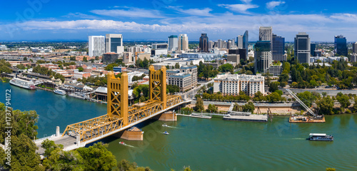 Aerial view of Sacramento, California, showing the golden Tower Bridge over the Sacramento River, downtown buildings, and the State Capitol surrounded by trees.