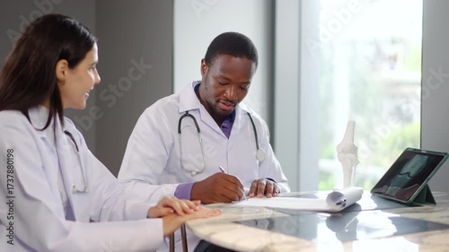 Two doctors engage in an important discussion about patient care at a clinic. They review documents and use a tablet computer for important health information and prescriptions, advice at hospital