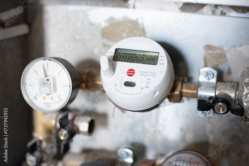 Close-up of a modern digital water meter with pressure gauge installed on a household pipe system. Concept of utility measurement, energy efficiency, infrastructure and resource control.