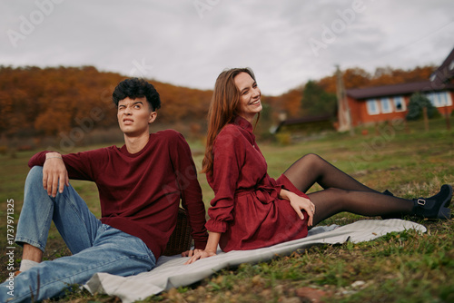 An authentic candid moment outdoors featuring a young couple relaxed on a blanket, wearing casual autumn attire, presenting genuine ease and a natural, spontaneous connection.