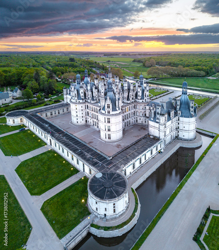 Aerial view of the ChÃ¢teau de Chambord, its formidable architecture reflecting in the surrounding moat, under the warm hues of the setting sun, Chambord, Centre-Val de Loire, France.