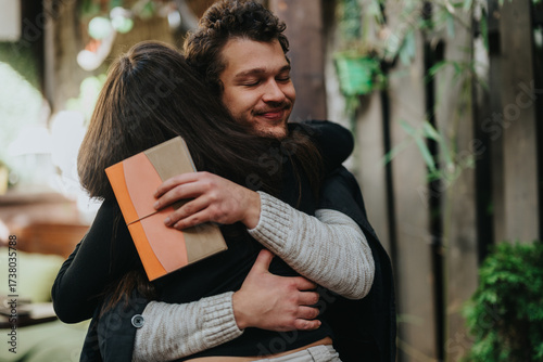 Man and a woman embracing warmly outdoors, with one holding a wrapped gift symbolizing affection and connection. The scene embodies love, sharing and emotional bonding in a comforting natural setting.