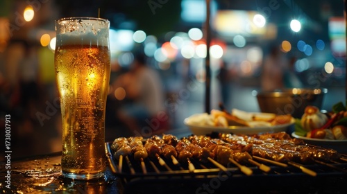 Cold Thai beer glass with condensation next to grilled skewers on a street food table.

