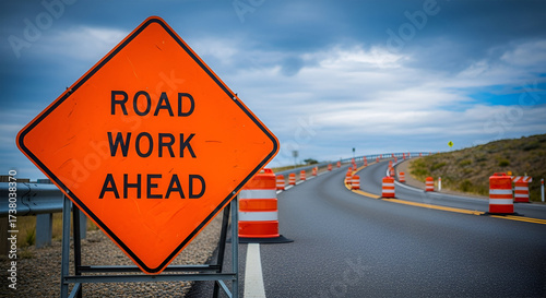 Road work ahead sign with orange cones lining the asphalt road under a cloudy sky.