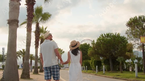 Young couple tourists walking hand in hand along Batumi promenade with palm trees and seaside view on sunrise, concept of tourism, vacation, lifestyle and romantic travel in Georgia