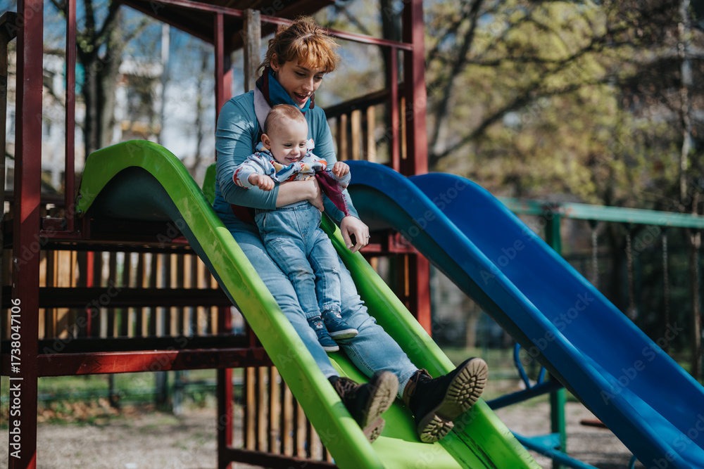 Obraz premium A woman and her child share a joyful moment sliding down a playground structure. Bonding, smiles, and laughter are captured in this vibrant outdoor scene under the sun.