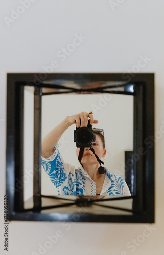 The girl takes a picture of herself in the mirror on the wall.