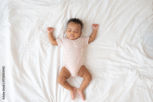 Top view of cute newborn baby sleeping and crib arms and legs on bed at home