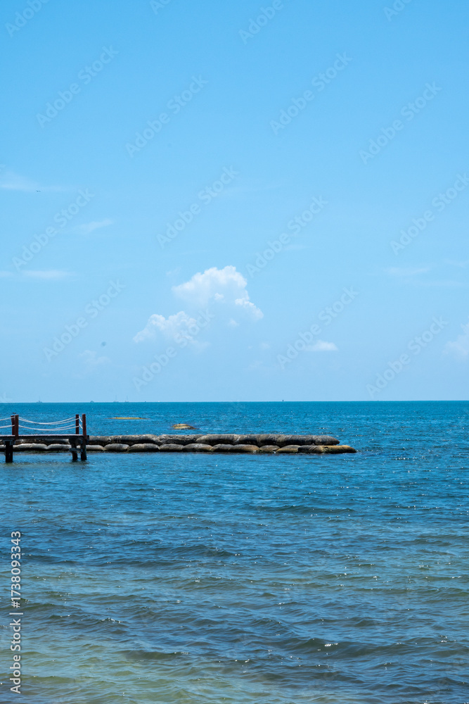 Obraz premium Wooden pier with stone breakwater in blue ocean under clear sky
