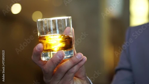 Elegant hand holding a glass of amber whiskey, showcasing the rich color and reflections, as the drink is gently swirled, capturing the essence of celebration and sophistication at a wedding event