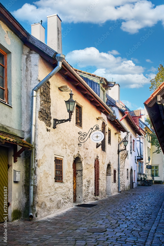 Obraz premium Medieval stone street with archways and rustic buildings in historic European town. Narrow cobblestone street with medieval stone walls, wooden doors and tiled archways in an old European town.