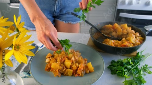 Woman serving cooked vegetables potatoes and chicken meat stew with parsley on plate on kitchen. Culinary techniques, homemade preparing healthy meal cook food, organic cuisine from fresh ingredients.