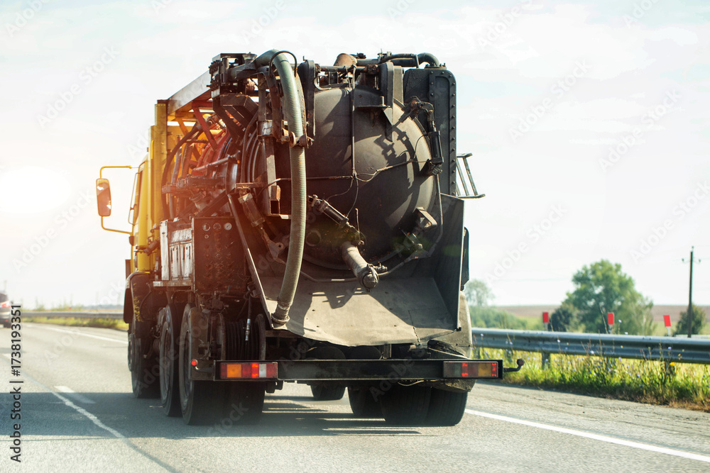 Naklejka premium A concrete mixer with a concrete delivery hose on a country road against the backdrop of the sunset. Copy space for text