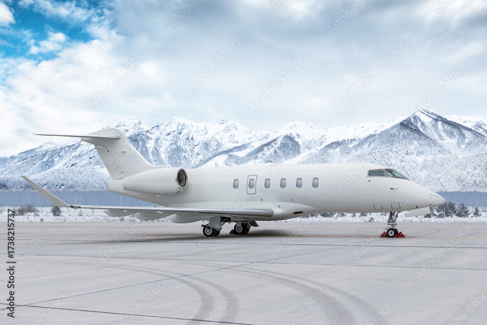 Naklejka premium White corporate airplane at winter airport on background of high scenic snow capped mountains