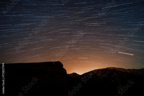 Long exposure photo shows star trails moving across the night sky above a dark mountain range.