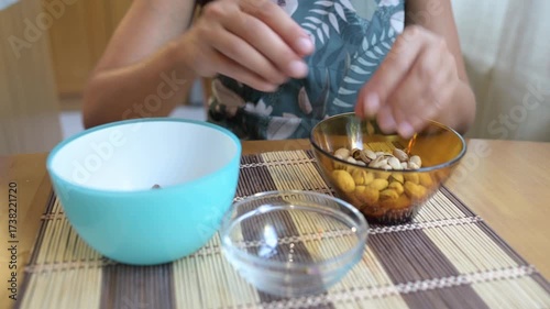 Hands shelling pistachios into bowls on a kitchen table, preparing a healthy snack at home