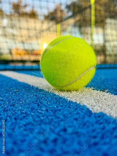 Paddle tennis ball close up on the white line of blue artificial outdoor court surface with a shallow depth
