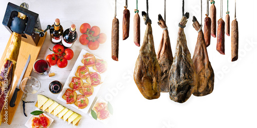 La mesa ibérica une tradición y sabor: jamón, vino y gesto culinario en escena compartida.Jamón en soporte, embutidos colgados, vino, pan con tomate, queso y tomates sobre mesa rústica.