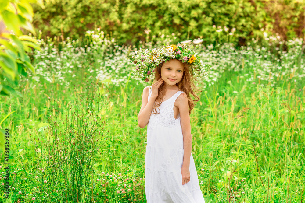 Obraz premium Cute smiling little girl with flower wreath on the meadow at the farm. Portrait of adorable small kid outdoor.