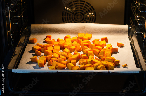 Roasted bright orange pumpkin cubes on baking paper in open oven
