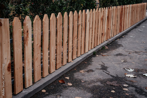 A wooden fence along the road. Fallen leaves on the sidewalk.
