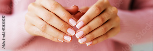 Classic French manicure highlights beautifully shaped nails, with a subtle pink hue and white tips. Hands rest gently together, showcasing a polished and elegant look in a serene setting