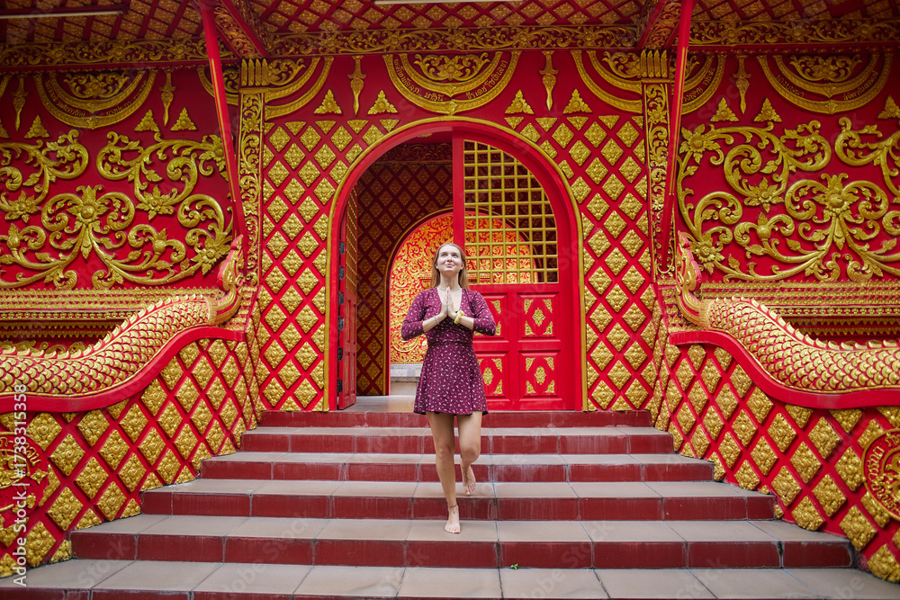 Fototapeta premium A Graceful Woman in a Purple Dress Offering a Gesture of Respect Amidst Vibrant Red and Gold Architectural Features