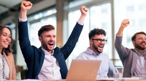 Group of four young professionals celebrating a successful project in a modern office environment