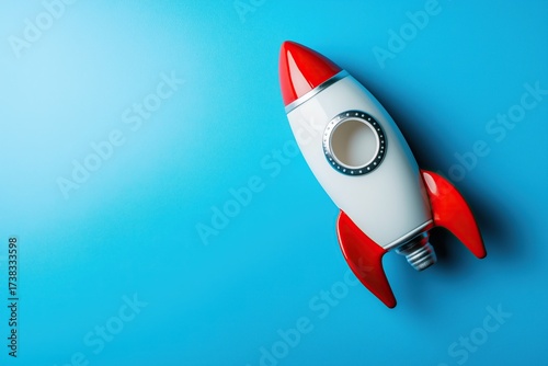 A red and white toy rocket lies flat on a textured light blue surface, shot from above