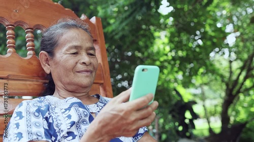 happy asian senior mature woman relaxing and using smartphone, speaking on mobile phone with family, thai asia elderly grandmother enjoy smart outdoor lifestyle with wireless technology device