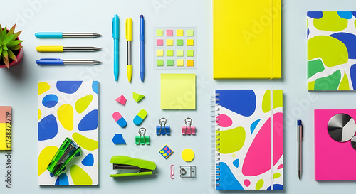 Overhead shot of a colorful and organized workspace featuring notebooks, pens, sticky notes, and decorative items arranged on a light blue surface, ideal for showcasing office or school supplies in a 