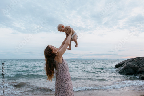 Fotografia Young caucasian woman playing with baby at beach during sunset