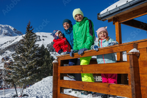 Family leans on balcony railing beneath bright midday winter sun
