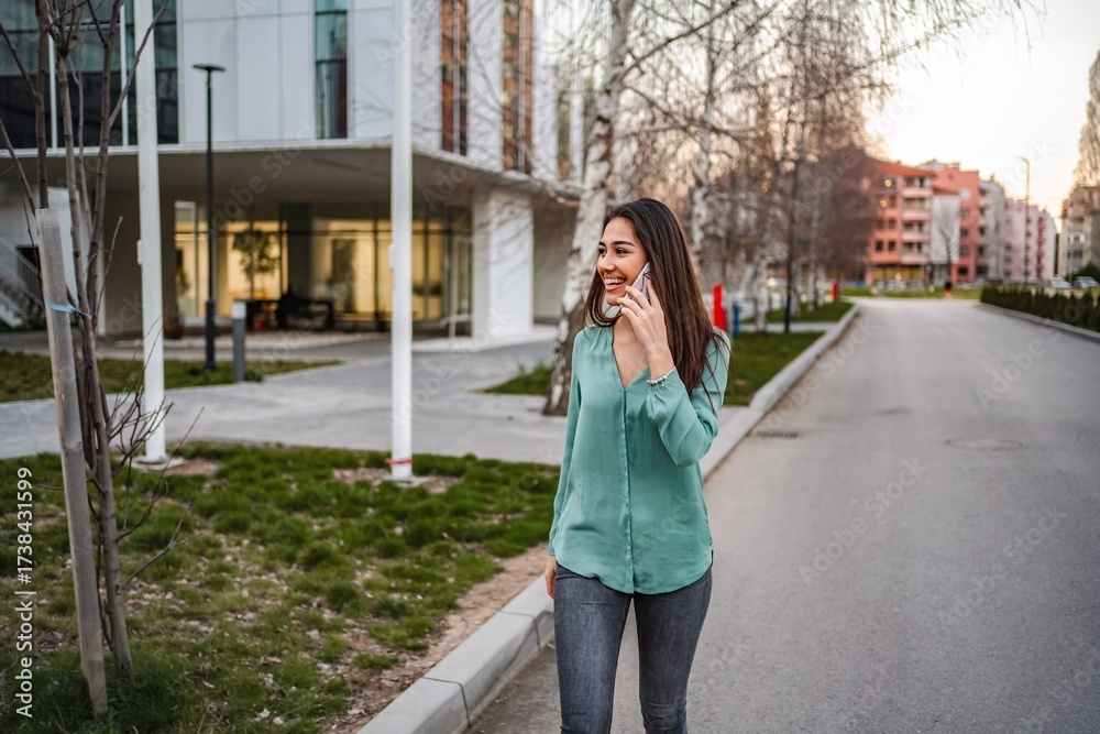 Fototapeta premium Young businesswoman walking down the street while talking on smartphone