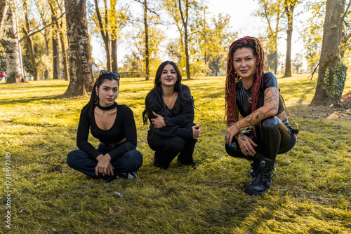 Diverse women with alternative fashion posing on grass, enjoying friendship in a park
