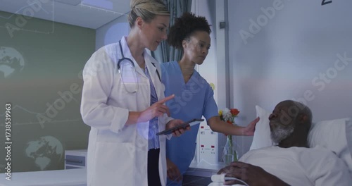 Doctor and nurse approaching hospital bed, tapping tablet and arranging flowers, comforting patient