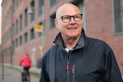 Portrait of a smiling senior man with eyeglasses waiting at a bus stop in the city