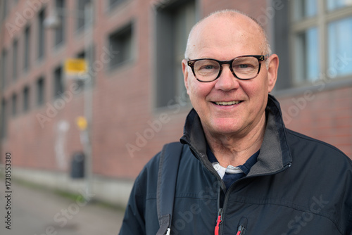 Portrait of a smiling senior man with eyeglasses waiting at a bus stop in the city