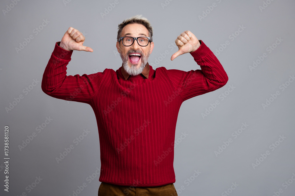 Fototapeta premium Cheerful businessman in casual red pullover pointing at himself and expressing happiness while posing against a solid background