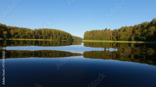 Adult person swims in a still lake surrounded by dense forest during summer evening, with serene reflections and natural tranquility in a remote nature setting