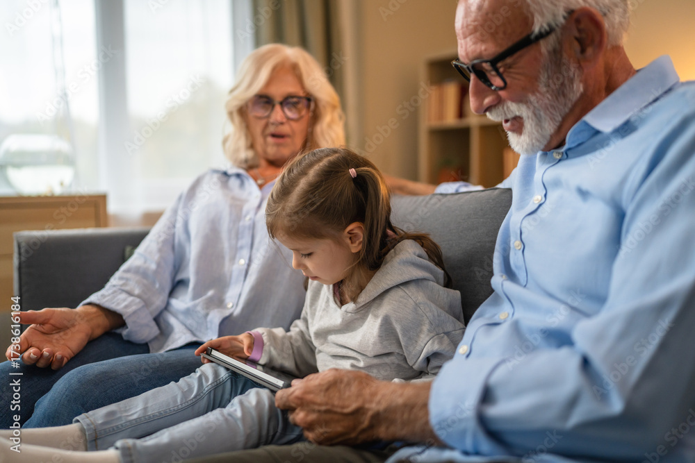 Obraz premium Grandchild using digital tablet with her grandparents at home