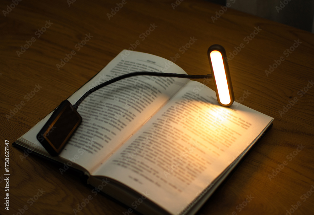 Fototapeta premium A convenient clip-on reading lamp with color options, placed over a book on the table for reading