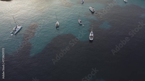 Aerial view of sailboats floating in the turquoise waters of Ibiza surrounded by deep blue sea patches