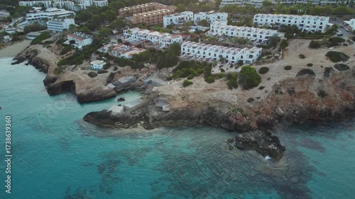 Aerial shot of a sandy beach in Ibiza with turquoise waters, resorts, and green hills in the background
