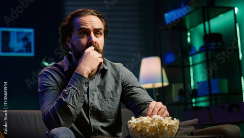 Obraz na plátně Puzzled man eating popcorn while watching confusing movie on streaming service, enjoying time off from work