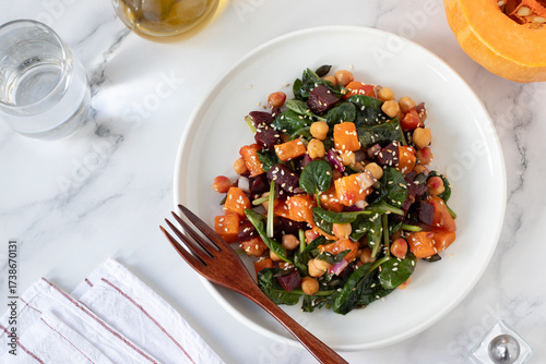 Vegan salad with pumpkin, beetroot, and chickpeas in a plate on white kitchen table. Top view.